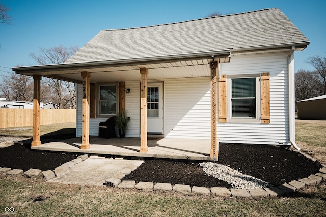 back of house with a porch, fence, and roof with shingles