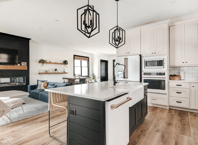 kitchen featuring white appliances, white cabinets, light countertops, an island with sink, and pendant lighting