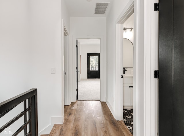 hall featuring light wood-style floors, baseboards, and visible vents