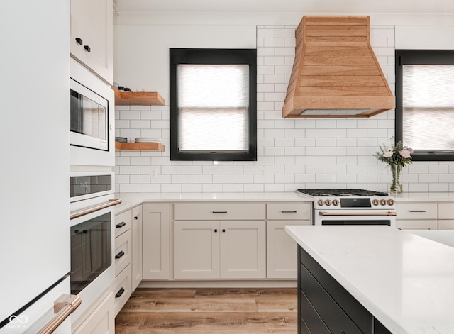 kitchen featuring white appliances, white cabinets, custom exhaust hood, light countertops, and open shelves