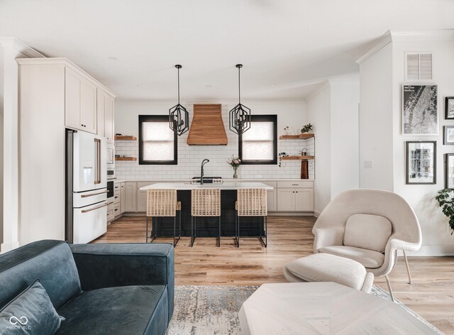 kitchen featuring a kitchen island with sink, white appliances, white cabinetry, light countertops, and decorative light fixtures