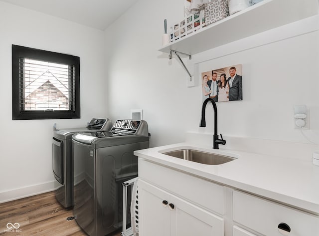 laundry area with a sink, baseboards, independent washer and dryer, cabinet space, and light wood finished floors