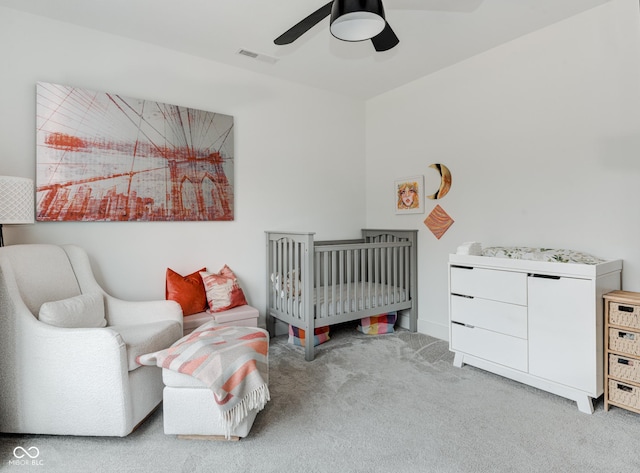 bedroom with light colored carpet, visible vents, ceiling fan, and a crib