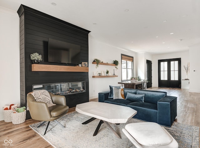 living room featuring a fireplace, wood finished floors, baseboards, french doors, and crown molding