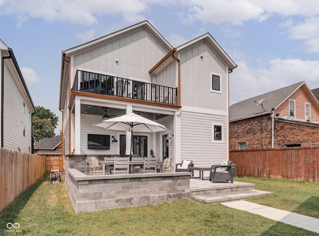 back of property with a lawn, a patio, a balcony, a fenced backyard, and board and batten siding