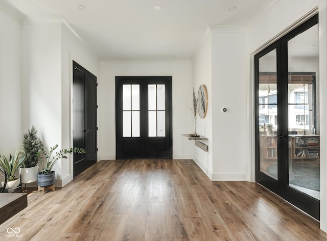 foyer with a wealth of natural light, french doors, crown molding, and light wood finished floors