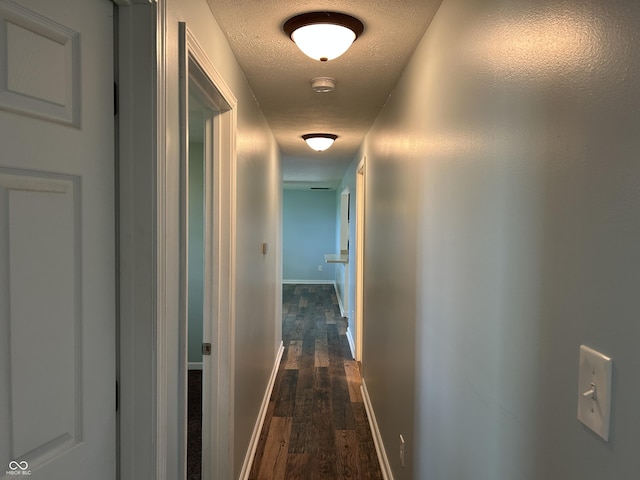 hallway featuring a textured ceiling, baseboards, and dark wood-type flooring