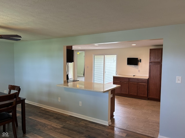 kitchen with stainless steel refrigerator, light countertops, a textured ceiling, baseboards, and wood finished floors