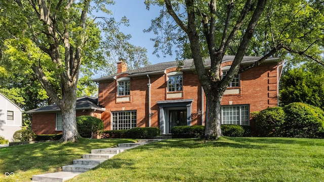 colonial home with brick siding, a chimney, and a front lawn