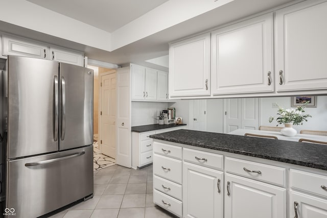 kitchen featuring light tile patterned floors, dark stone counters, white cabinets, and freestanding refrigerator