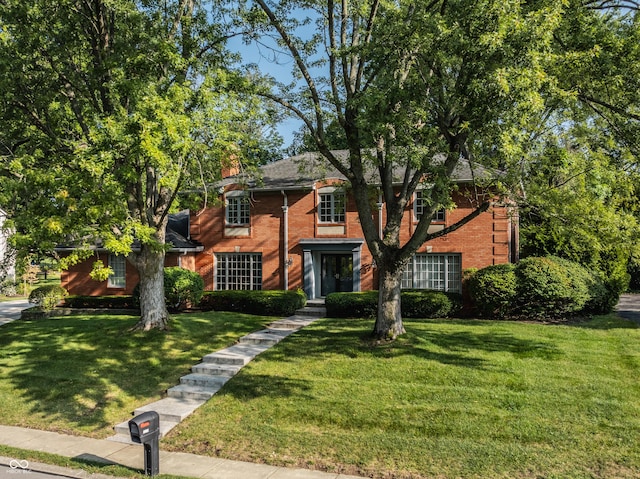 colonial house featuring brick siding, a chimney, and a front yard