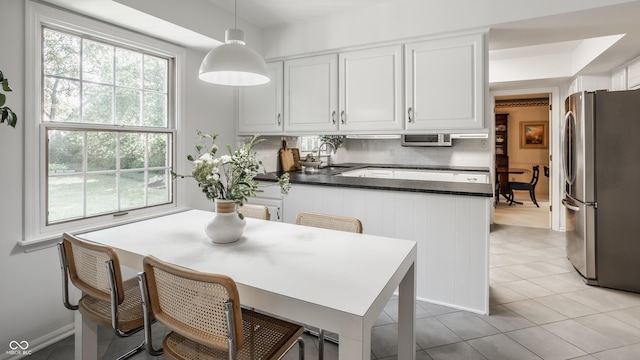 kitchen with dark countertops, decorative backsplash, a peninsula, freestanding refrigerator, and a sink