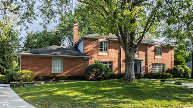 view of front of house featuring brick siding, a chimney, and a front lawn