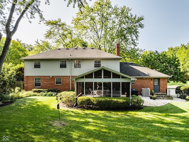 rear view of property with a sunroom, a chimney, central air condition unit, a lawn, and brick siding