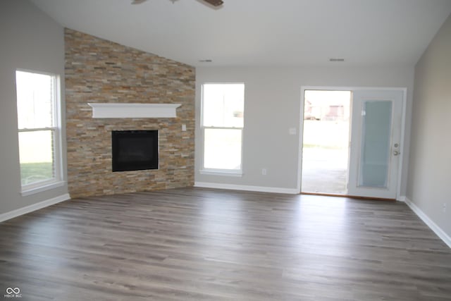 unfurnished living room with vaulted ceiling, a stone fireplace, a healthy amount of sunlight, and dark wood-type flooring