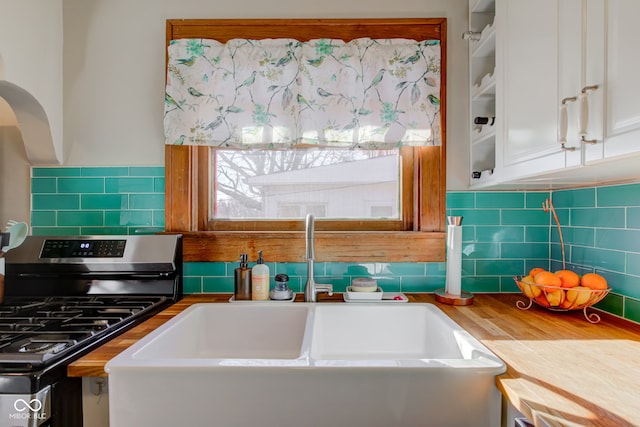 kitchen featuring butcher block countertops, sink, backsplash, white cabinets, and gas range