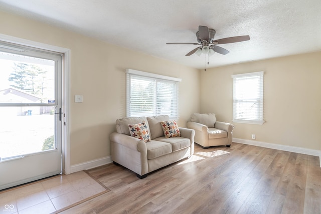 living room with ceiling fan, a textured ceiling, and light wood-type flooring