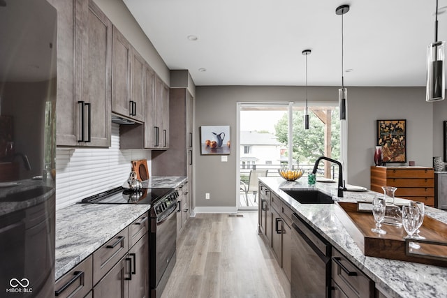 kitchen featuring sink, black appliances, hanging light fixtures, light stone countertops, and backsplash