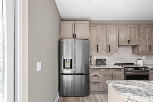 kitchen with tasteful backsplash, appliances with stainless steel finishes, light stone countertops, and light hardwood / wood-style flooring