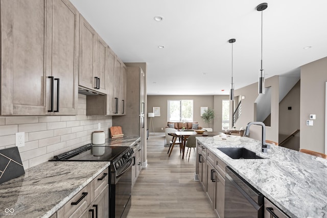 kitchen featuring light brown cabinetry, sink, light stone counters, decorative light fixtures, and black appliances