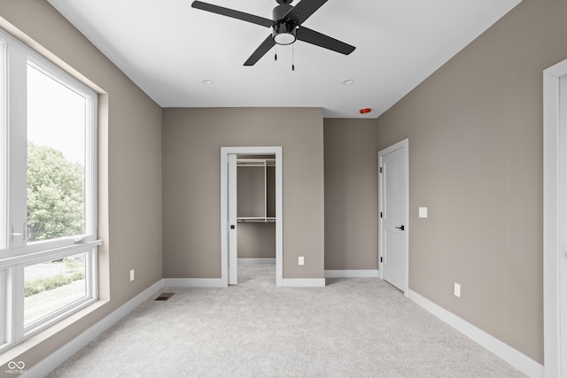 unfurnished bedroom with a spacious closet, light colored carpet, a closet, and ceiling fan