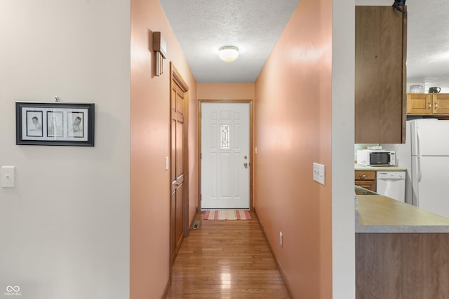 corridor featuring light wood-style flooring, a textured ceiling, and baseboards