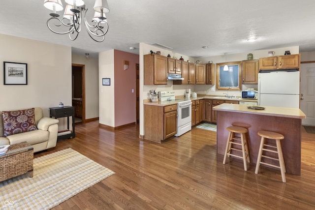 kitchen featuring under cabinet range hood, white appliances, wood finished floors, light countertops, and brown cabinetry