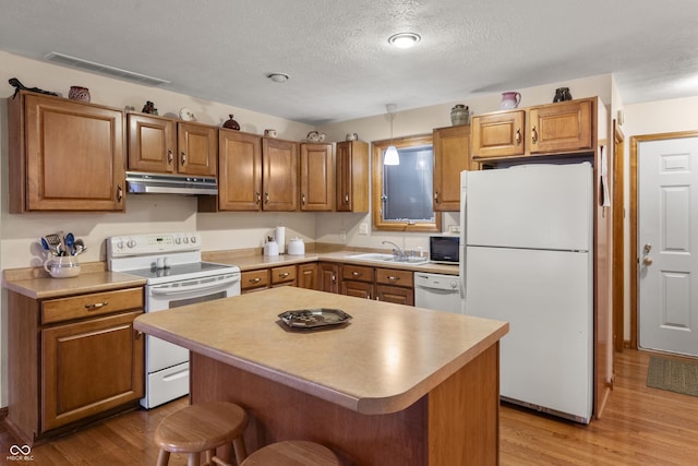 kitchen with white appliances, visible vents, light wood-style floors, under cabinet range hood, and a kitchen bar