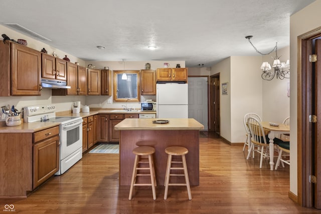 kitchen with a center island, brown cabinets, wood finished floors, white appliances, and under cabinet range hood