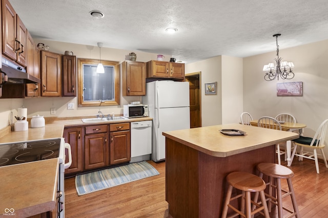 kitchen with light wood finished floors, hanging light fixtures, white appliances, and a kitchen breakfast bar