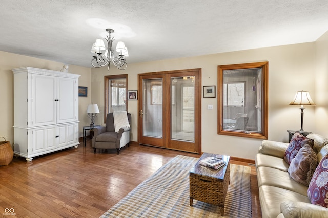 living area featuring a chandelier, a textured ceiling, wood finished floors, and baseboards