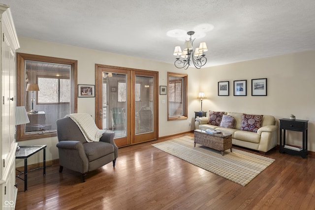 living area featuring a textured ceiling, a notable chandelier, dark wood-type flooring, baseboards, and french doors