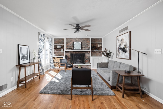 living area with wood finished floors, visible vents, built in features, ornamental molding, and a brick fireplace