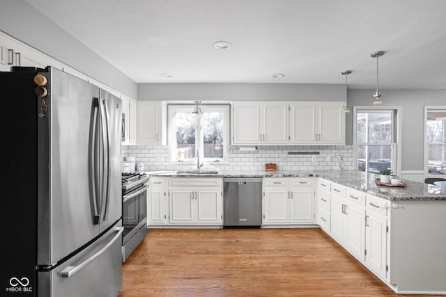 kitchen with a peninsula, a sink, white cabinetry, light wood-style floors, and appliances with stainless steel finishes