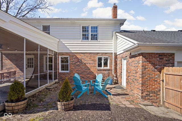 rear view of house with brick siding, a sunroom, roof with shingles, a chimney, and a patio area