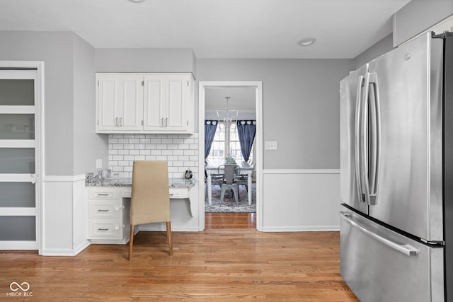 unfurnished office featuring a wainscoted wall, light wood-style flooring, and built in desk