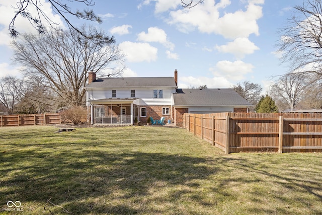 rear view of property featuring a chimney, brick siding, a yard, and a fenced backyard