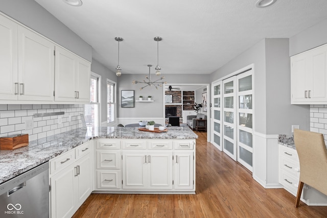 kitchen with light stone counters, light wood finished floors, white cabinets, dishwasher, and a peninsula