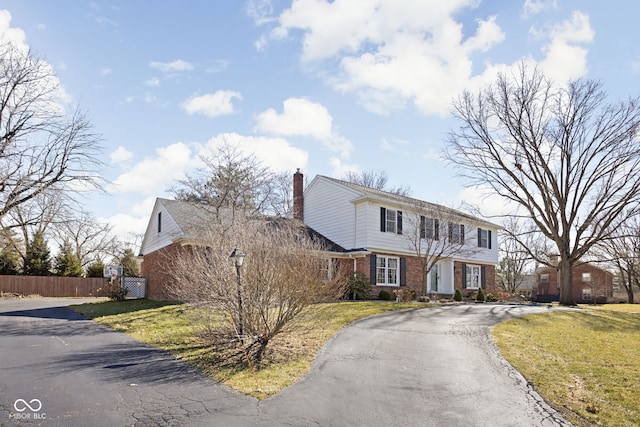 colonial house featuring brick siding, a chimney, a front yard, fence, and driveway