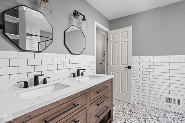 full bath with double vanity, a sink, visible vents, and tile walls