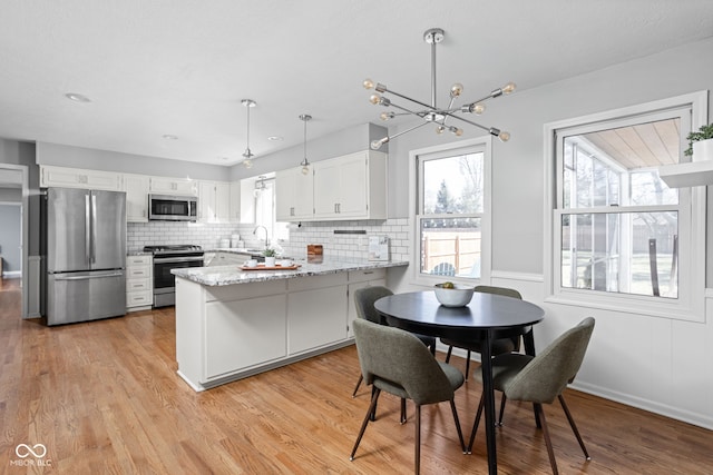 kitchen featuring appliances with stainless steel finishes, white cabinets, light wood-style flooring, and a peninsula