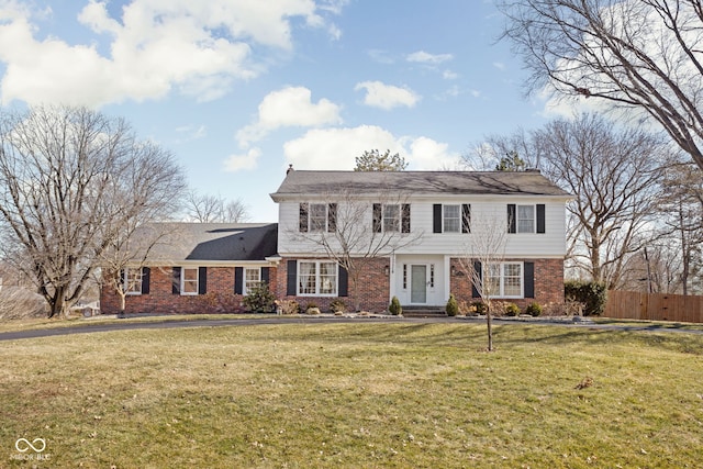 colonial inspired home with brick siding, a front yard, and fence