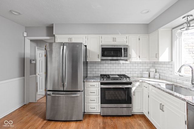 kitchen featuring appliances with stainless steel finishes, a sink, light wood finished floors, and light stone counters