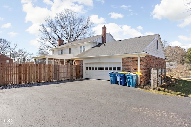 view of side of home with a garage, brick siding, fence, driveway, and a chimney