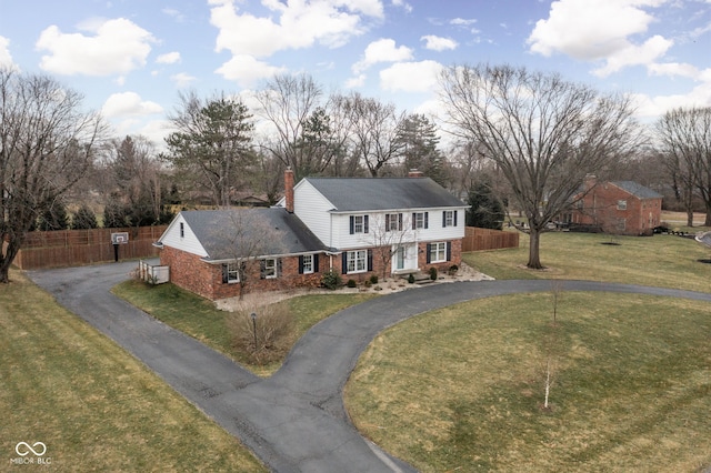 colonial house featuring driveway, a chimney, and brick siding