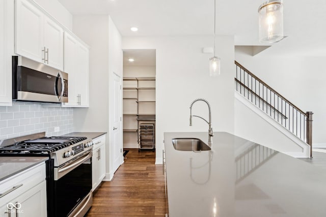 kitchen with pendant lighting, dark wood finished floors, stainless steel appliances, white cabinets, and a sink