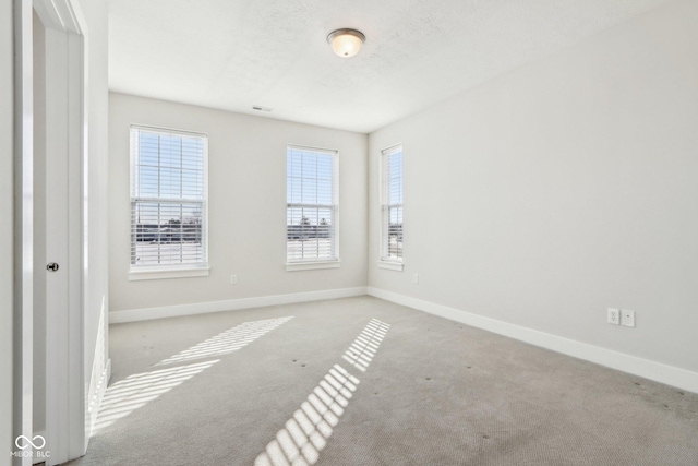 unfurnished room with light carpet, plenty of natural light, a textured ceiling, and baseboards