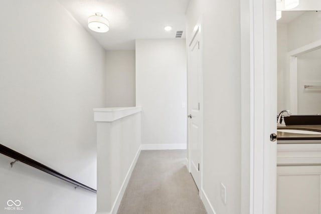 hallway featuring light colored carpet, visible vents, a sink, an upstairs landing, and baseboards