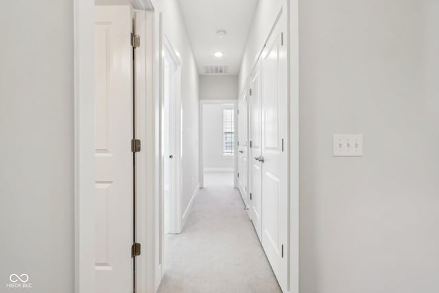 corridor with light carpet, baseboards, and visible vents