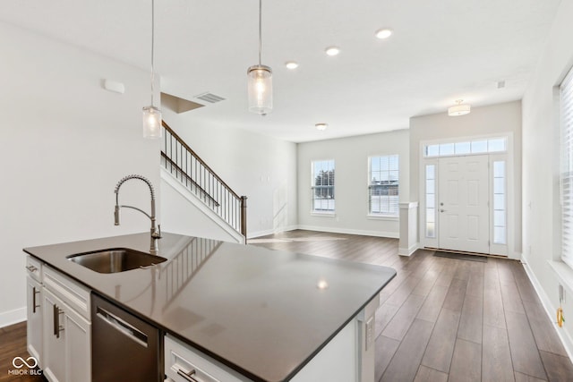 kitchen with a kitchen island with sink, a sink, hanging light fixtures, dishwasher, and dark countertops